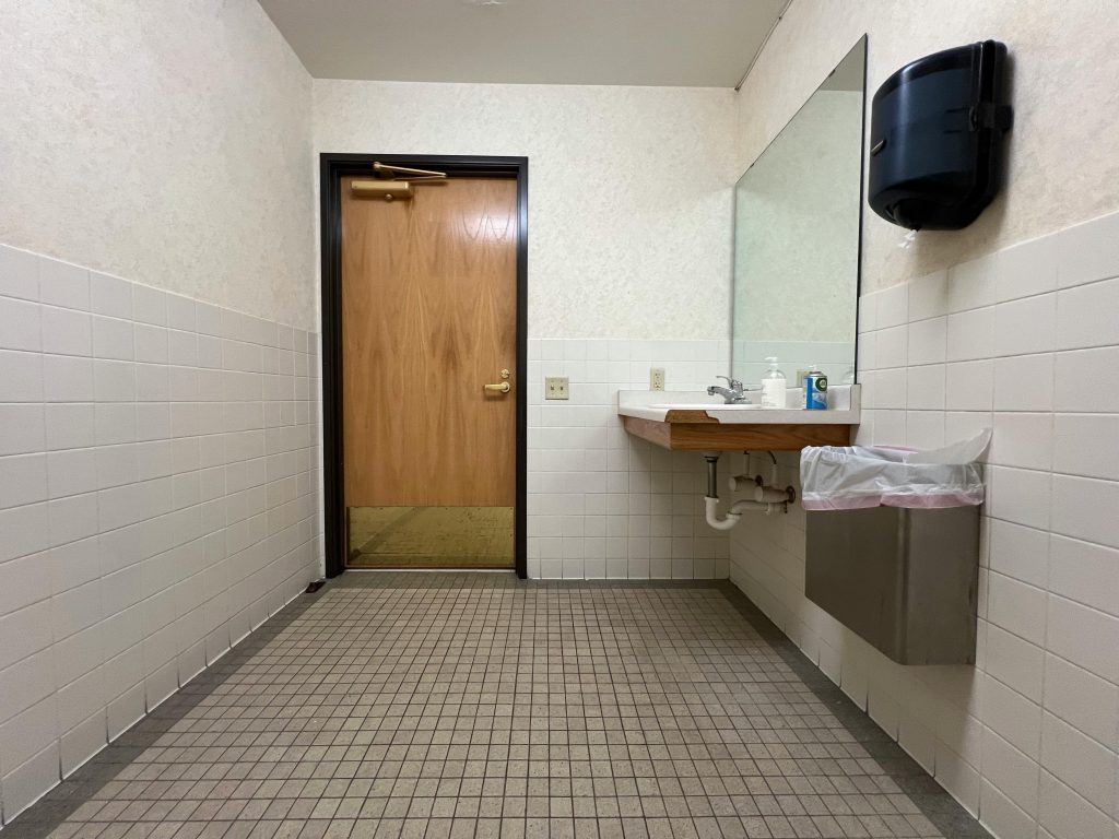 pexels-photo-20846593-20846593 Modern public restroom interior with a handbasin, mirror, and wooden door.